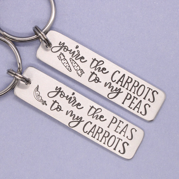Two silver keychains with engraved text on a light purple background
