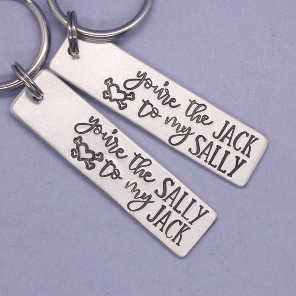 Two silver keychains text "You're the jack to my sally" and "You're the sally to my jack" on a purple background