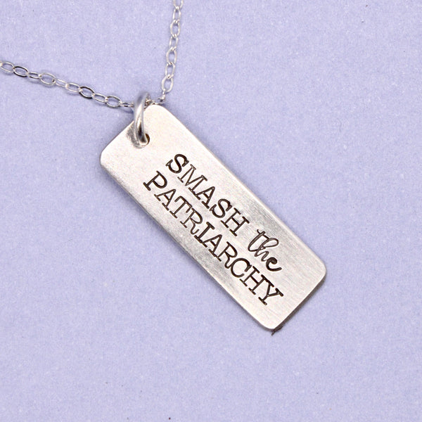 Silver necklace with 'SMASH THE PATRIARCHY' pendant on a light purple background