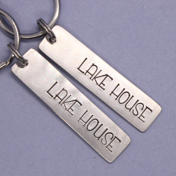 Two silver keychains with 'Lake House' text on a purple background