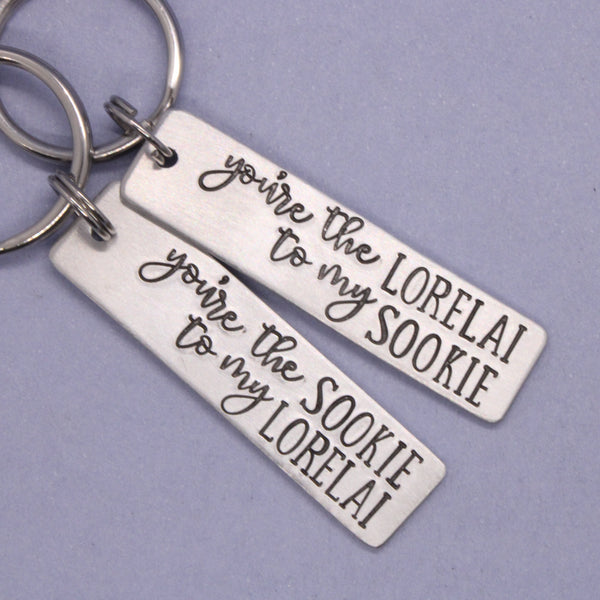 Two silver keychains with engraved text on a purple background