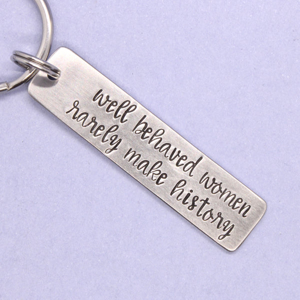 Silver keychain with engraved text on a light purple background